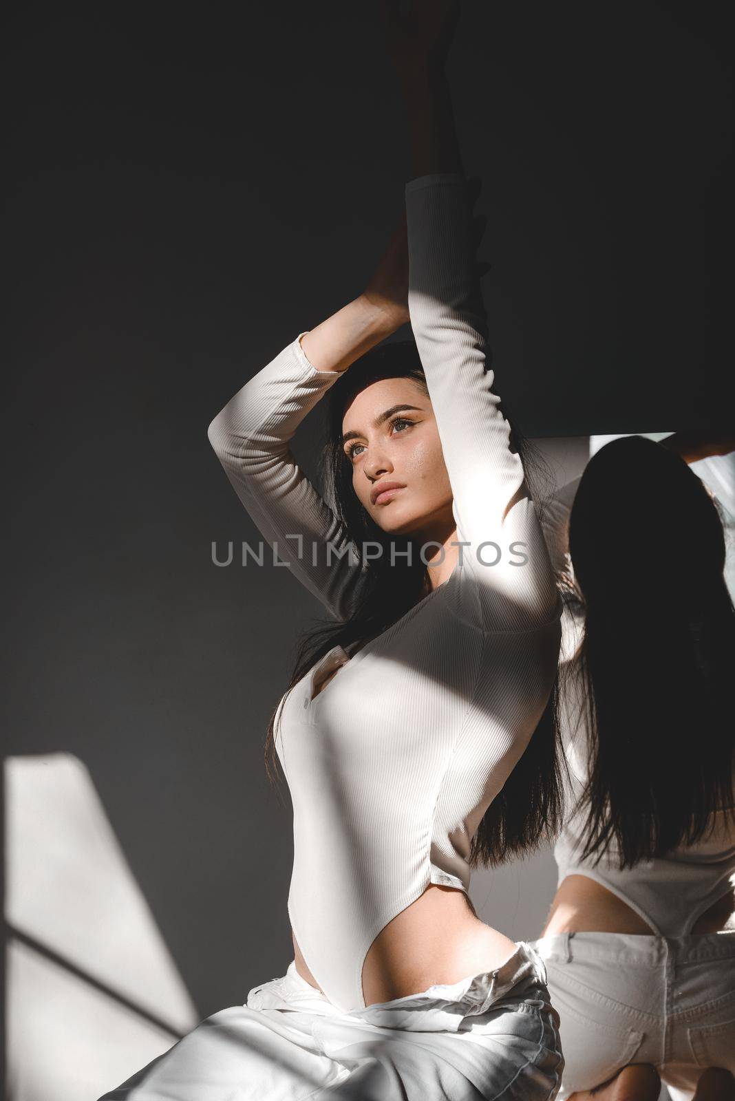 portrait of beautiful gentle woman in a white bodysuit posing in the sunshine. Black long hair. sensuality and tenderness.