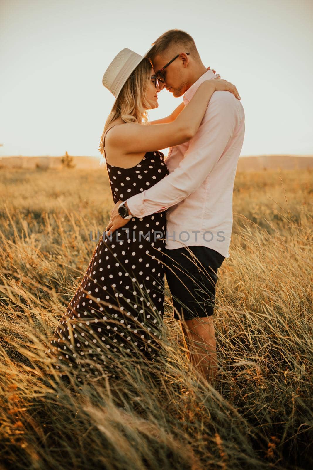 A man with a woman in a hat hug and kiss in the tall grass in the meadow by AndriiDrachuk