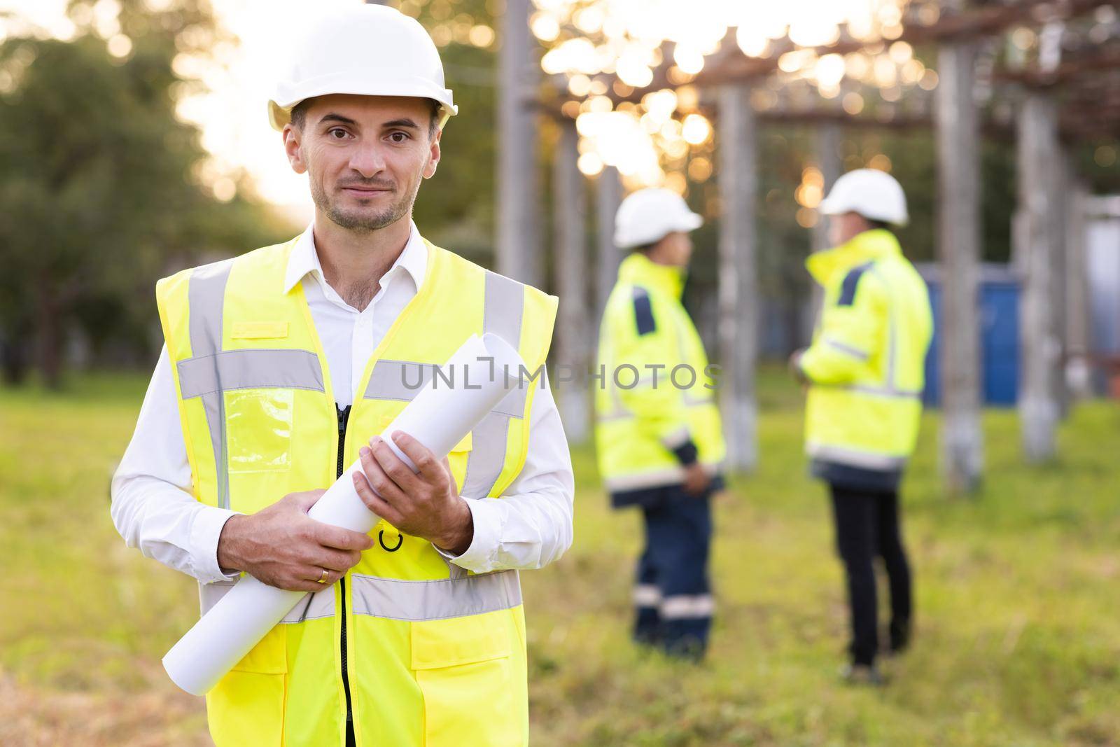 Portrait of engineer. Professional electrical industry engineer smiling and looking at the camera . Workers wearing safety uniform and hard hat with high voltage electrical lines background.