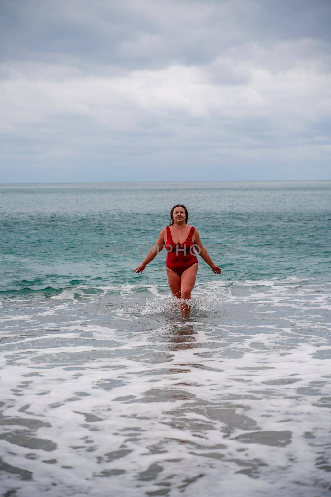 Woman in a bathing suit at the sea. A fat young woman in a red swimsuit enters the water during the surf by Matiunina