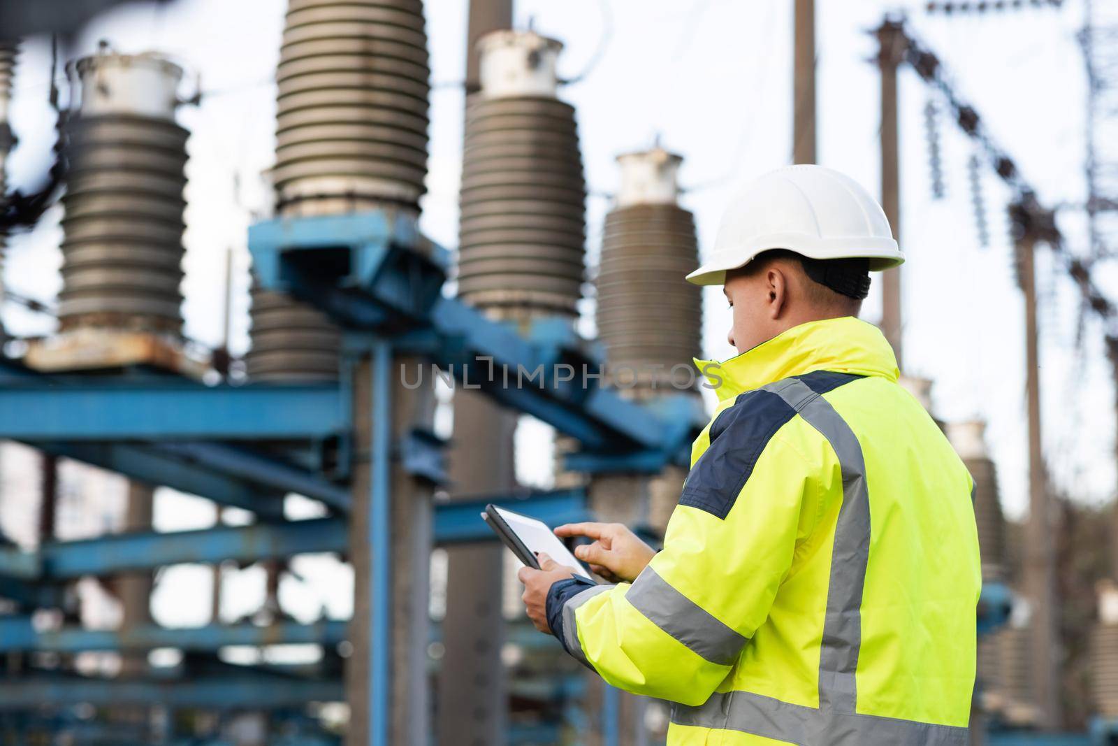 Electrical engineer studying reading on tablet. Electrical worker engineer a working with digital tablet, power near tower with electricity. Energy business technology industry concept by uflypro