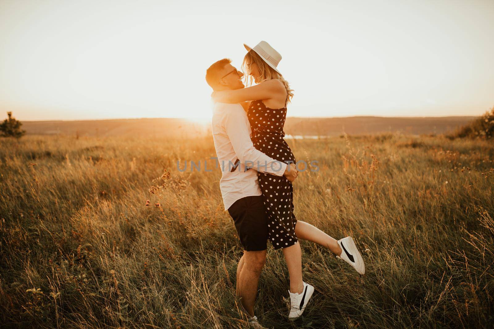 A man with a woman in a hat hug and kiss in the tall grass in the meadow by AndriiDrachuk