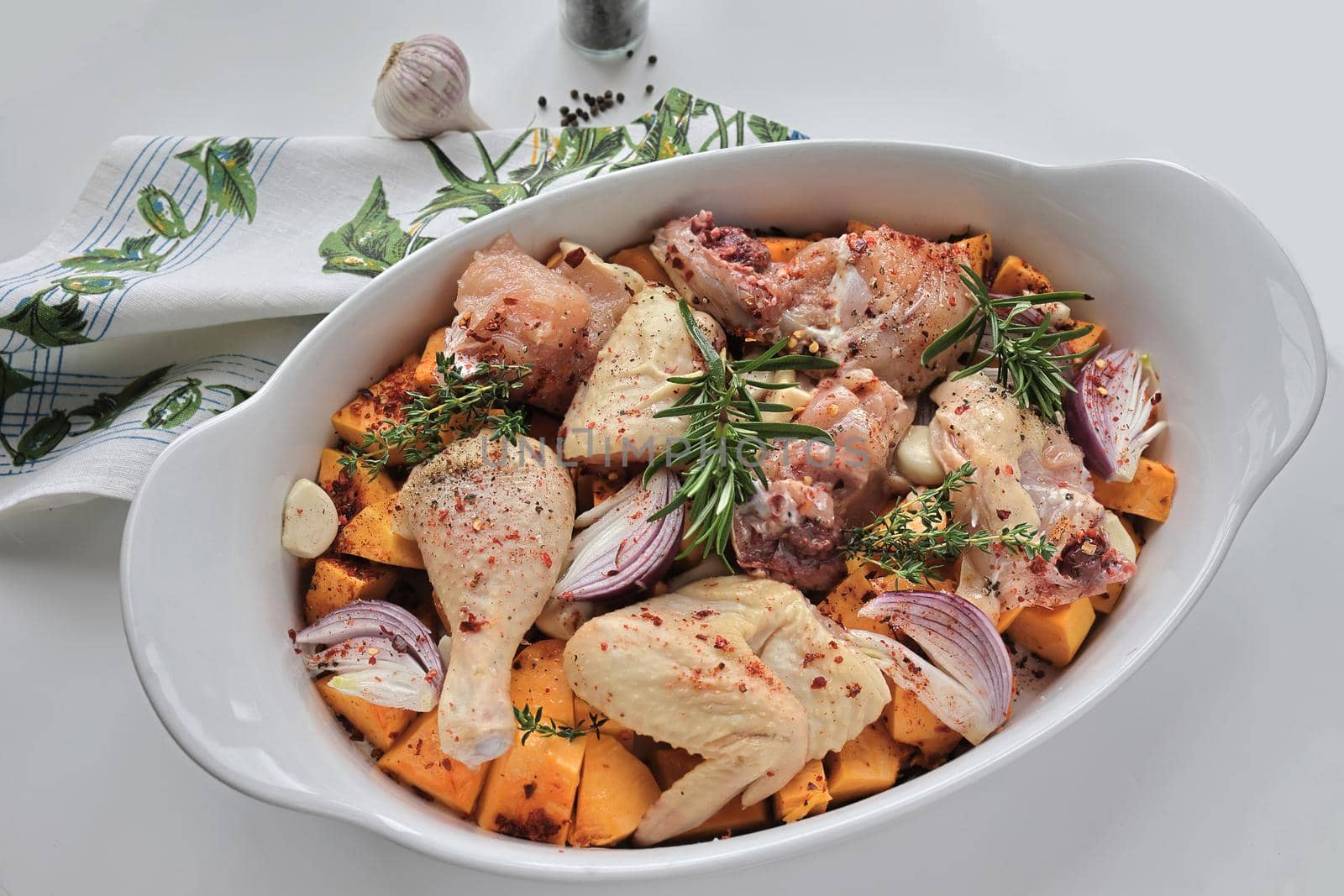 Chicken pieces prepared with pumpkin, onion, garlic and spices in a white ceramic baking dish. Decorated with rosemary. Autumn food concept. View from above. Flat lay