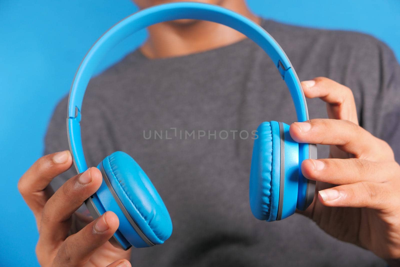Man hand holding headphone on blue background .