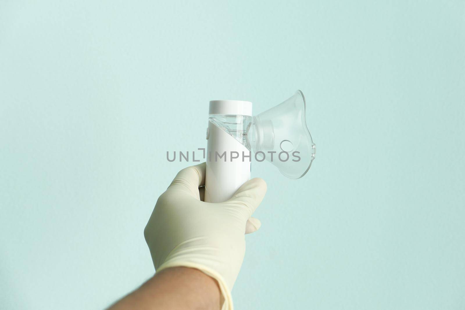 hand in latex gloves golding nebulizer against light green background .