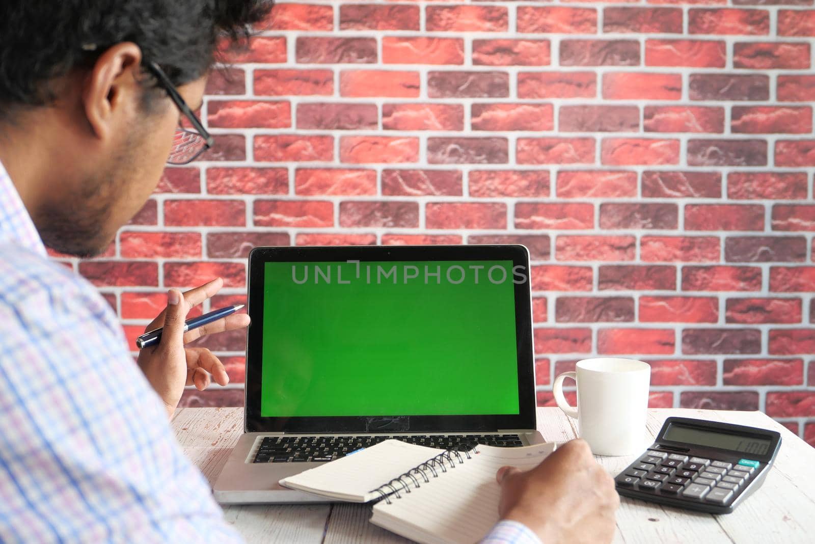 rear view of young man using laptop with blank screen on office desk