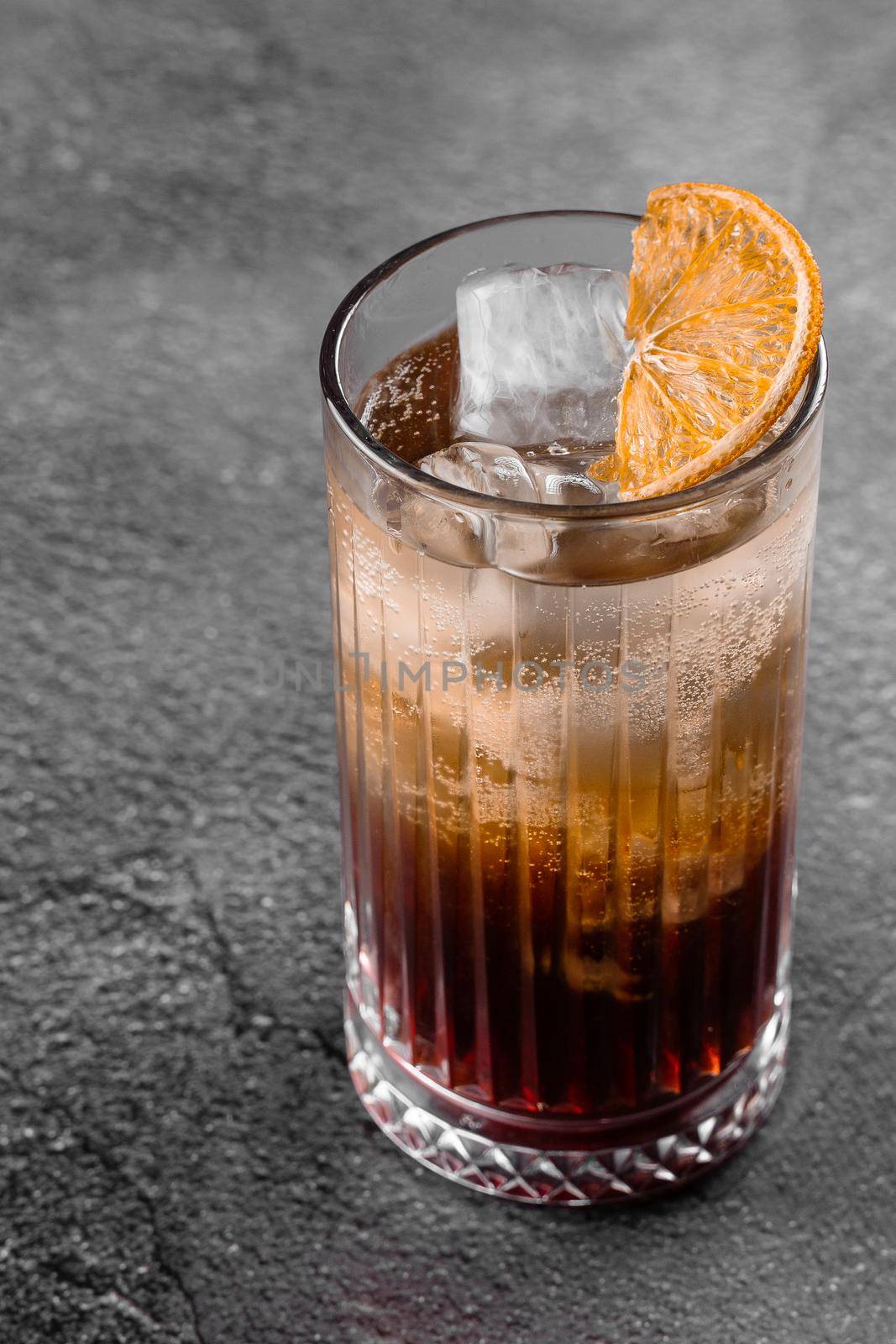 Cocktail in glass with cola, alcohol, ice, decorated dried orange on gray background