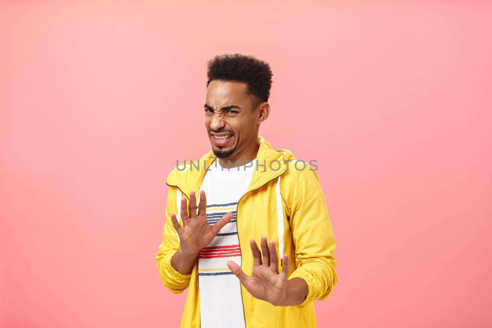 Guy prefers staying out of troubles. Disgusted displeased handsome dark-skinned man with afro hairstyle wrinkling nose and clenching teeth in disgust raising hands in rejection or refusal from dislike. Copy space
