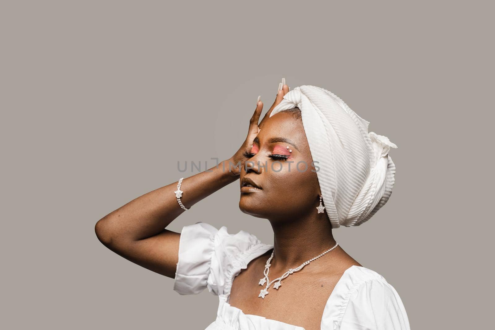 Beauty portrait of black muslim woman weared white dress and headscarf on gray background. Softness and wellness of body and skin