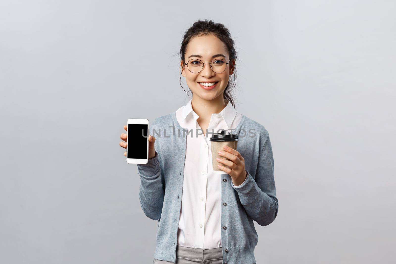 Office lifestyle, business and people concept. Young enthusiastic female teacher or tutor recommend use smartphone application to study during quarantine, drinking coffee, smiling show mobile phone.