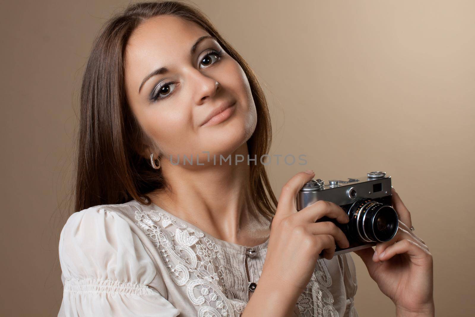 Young brown haired woman in beautiful dress holding retro camera in hands on neutral warm background