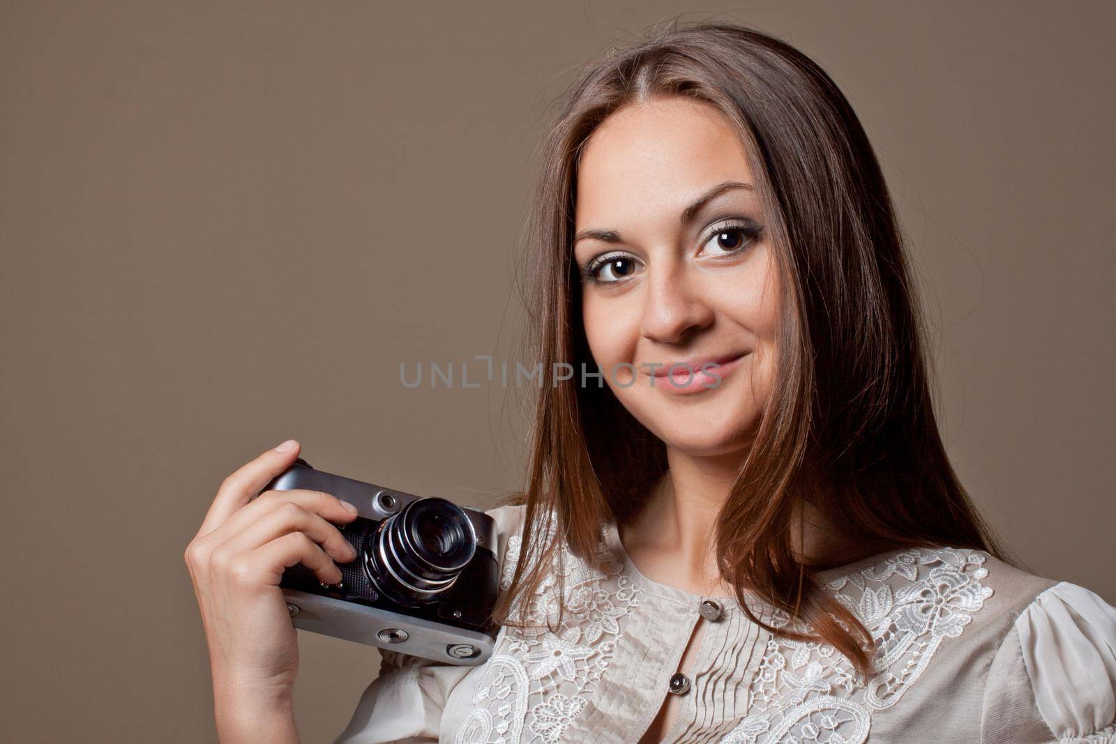 Young brown haired woman in beautiful dress holding retro camera in hands on neutral warm background