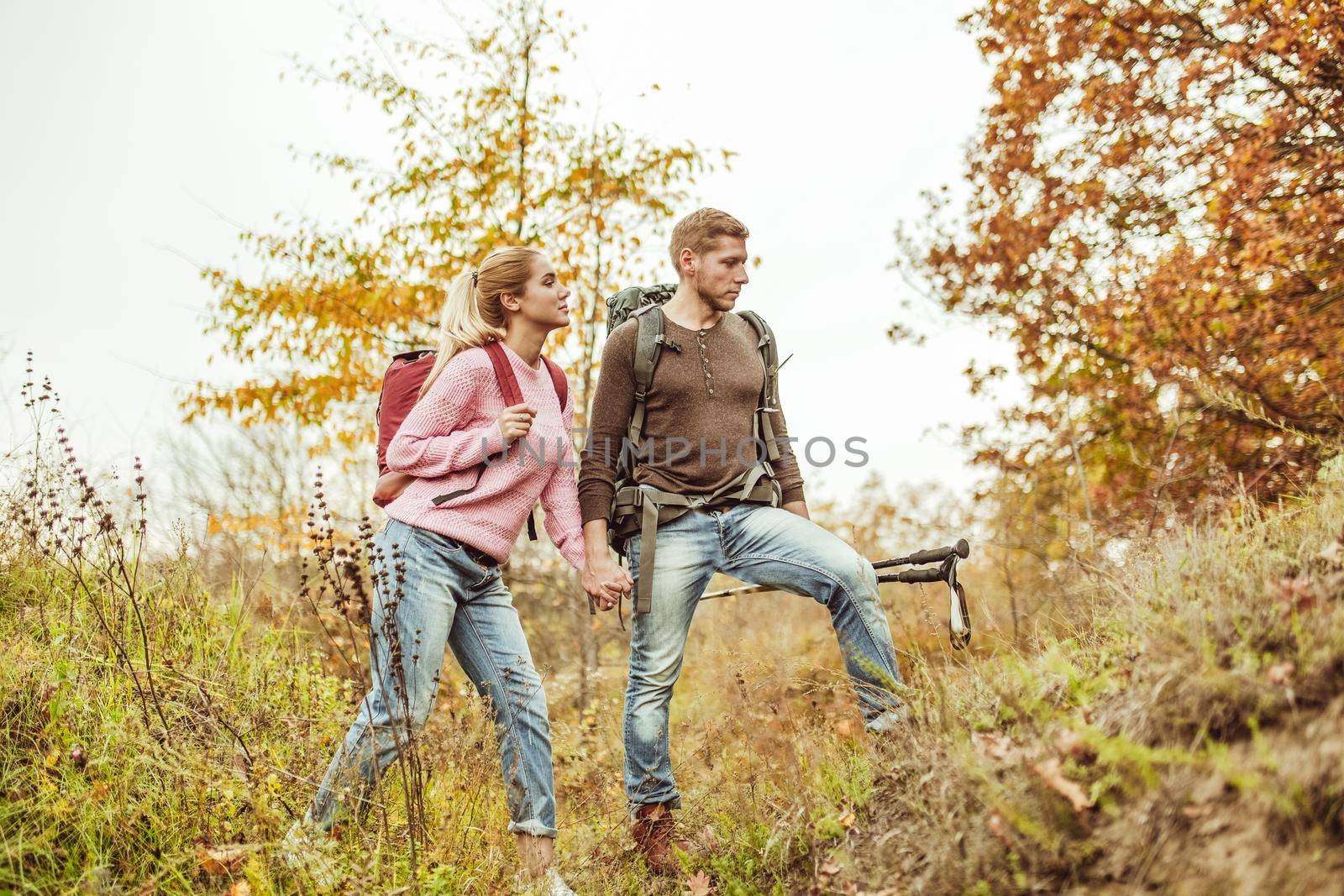 Tourists wading through the hills holding hands. A young couple of people in love checks the strength of their relationship while traveling in the wild. Hiking concept.