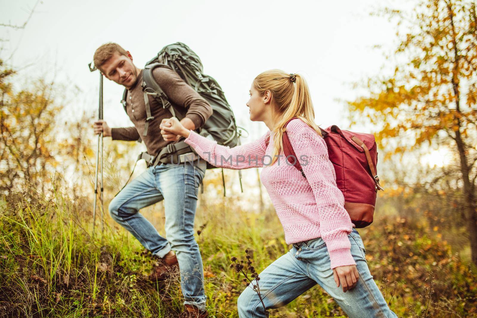 Man helps a woman climb a hill holding woman's hand and hiking poles in other hand. Hiking concept. Support and assistance concept.