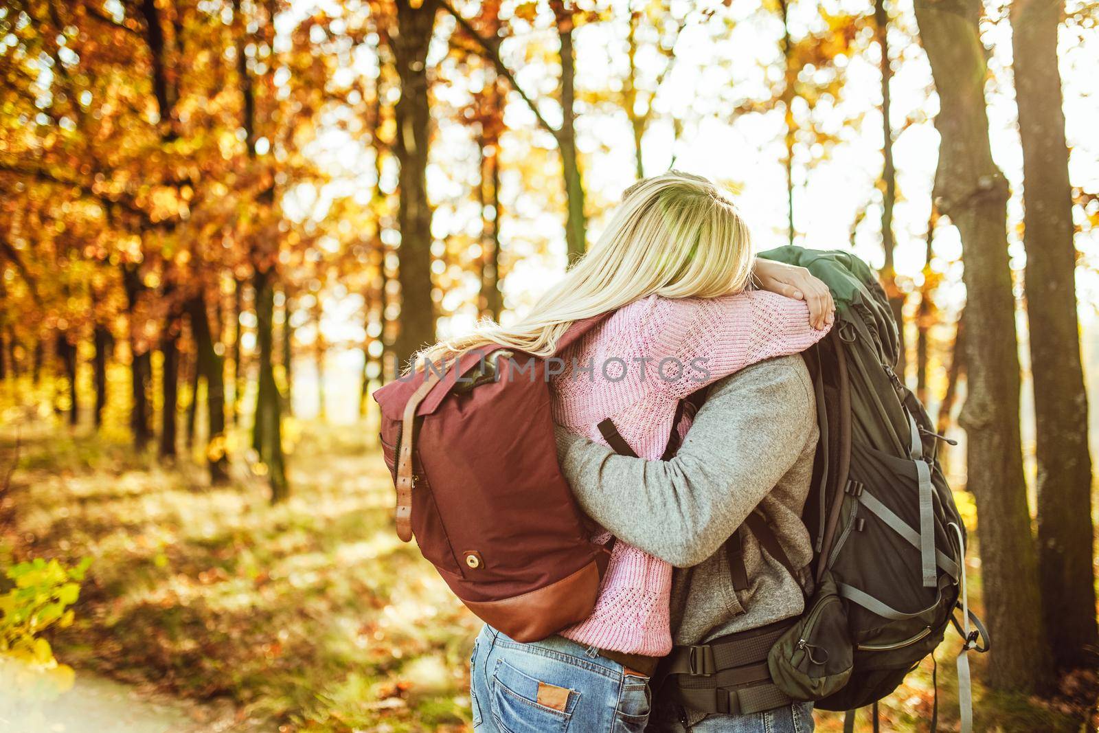 Embrace of couple of travelers, Man and woman with backpacks hugging while standing in the autumn forest. Copy space at left side.