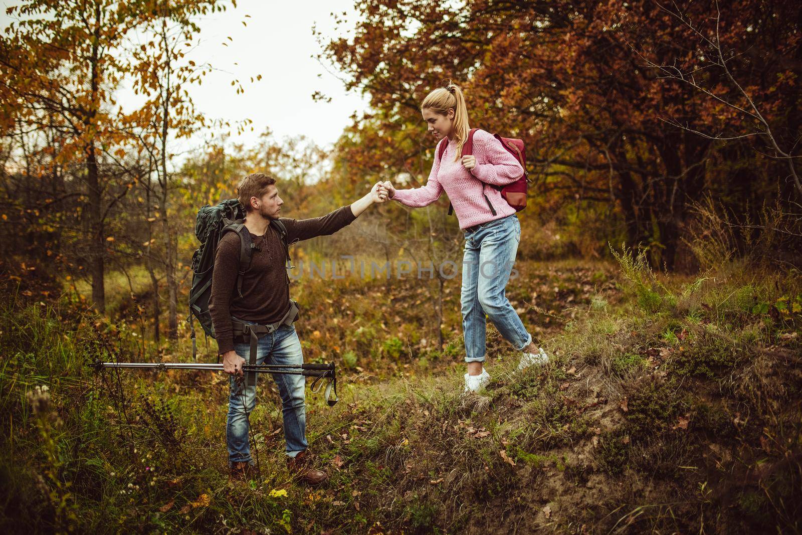 Intelligent tourist supports his woman on a hill descent. A man holds a woman's hand while supporting her on a difficult walking route. Hiking concept by LipikStockMedia