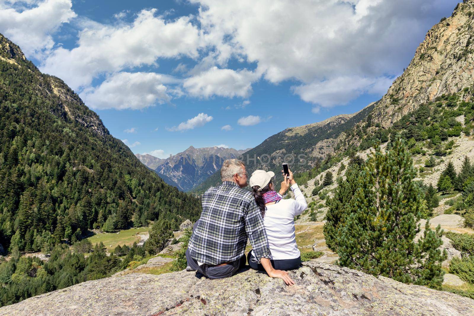 Middle aged tourist couple take a picture with mobile phone in Pyrenees mountain, Saint Maurici and Augestortes, Spain by Digoarpi