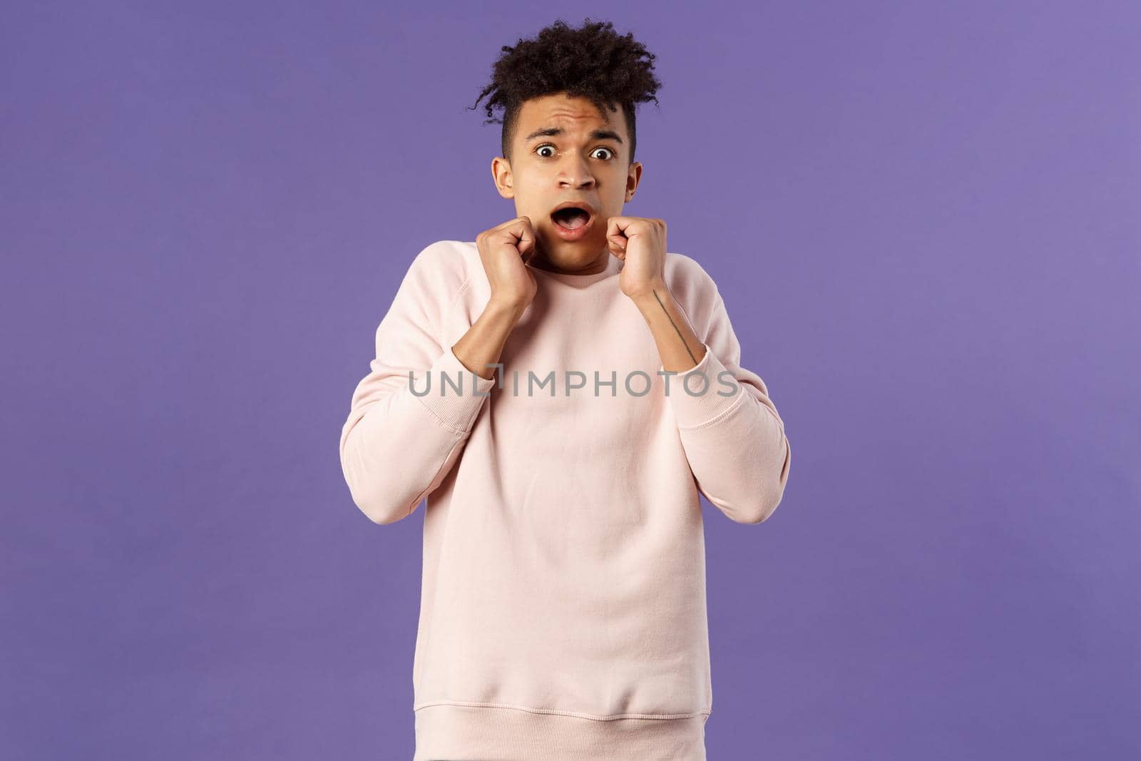 Portrait of scared hispanic guy screaming from fright, hold hands near face, open mouth gasping express fear and terrified emotion from watching horror movie, terrible accident, purple background by Benzoix
