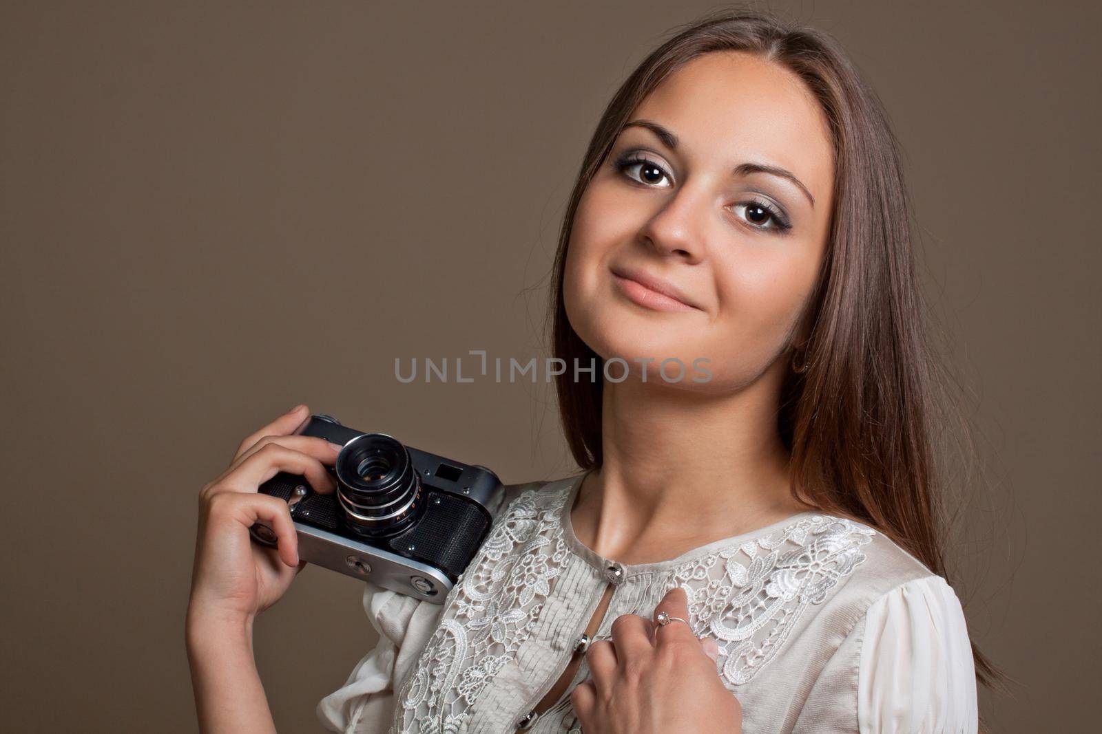 Young brown haired woman in beautiful dress holding retro camera in hands on neutral warm background