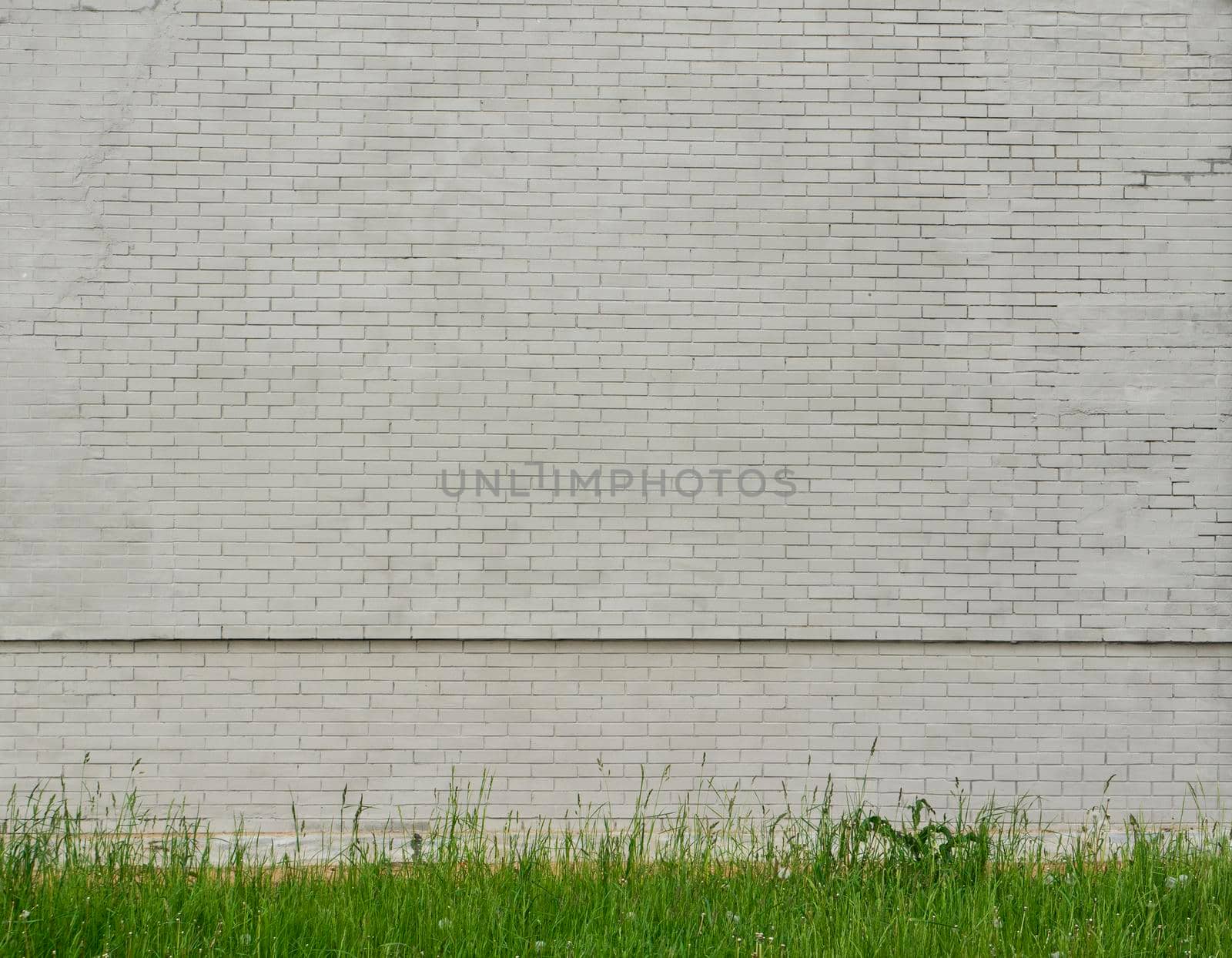 Old shabby gray brick wall of a building with green grass underneath. Brick wall and grass background.