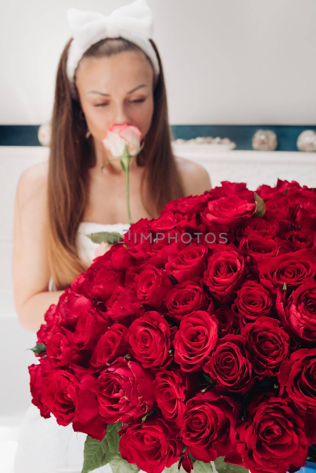 Close-up of bunch of stunning red roses and unrecognizable woman with flower in blurred background.