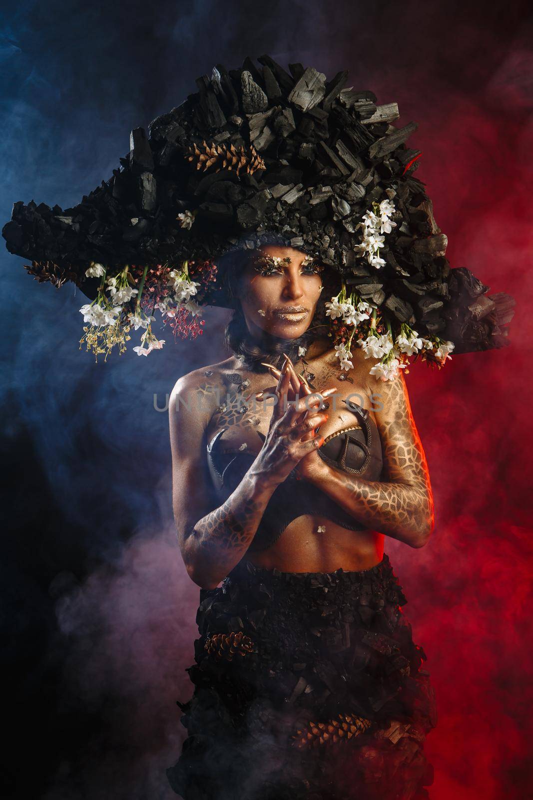 Portrait of a model in a headdress and dress made of coal. There is red smoke behind the model.