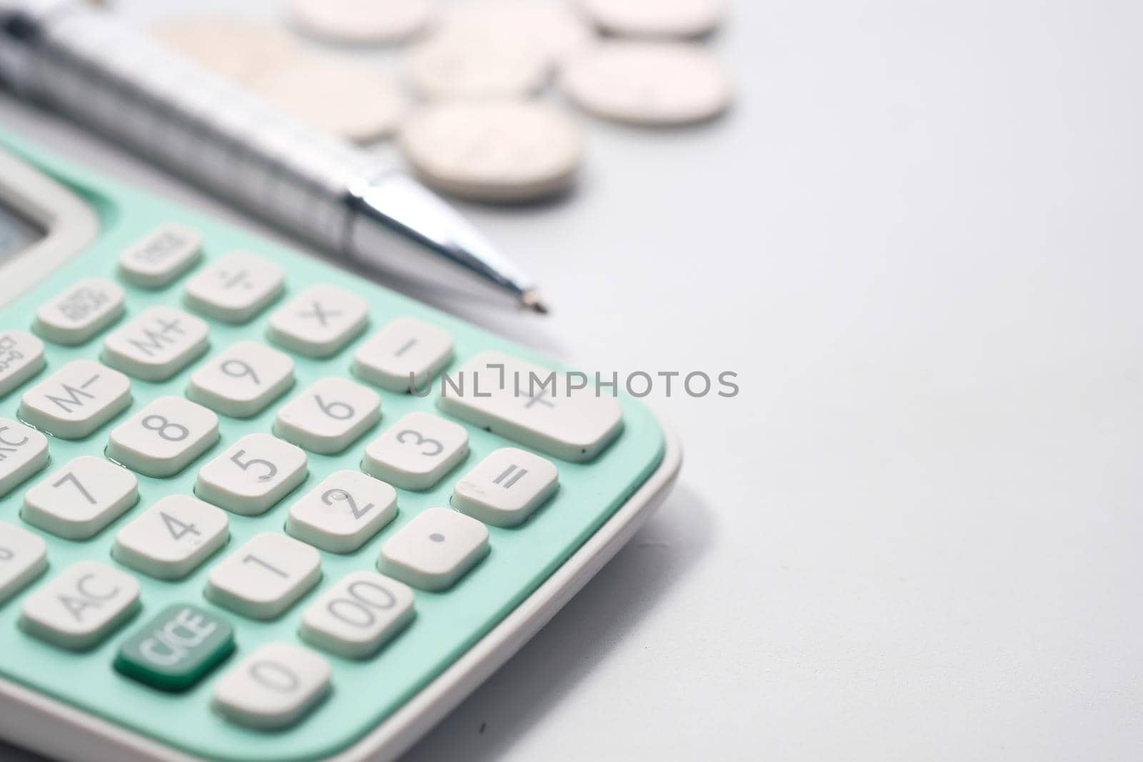 Close up of calculator, pen and coins on white background .