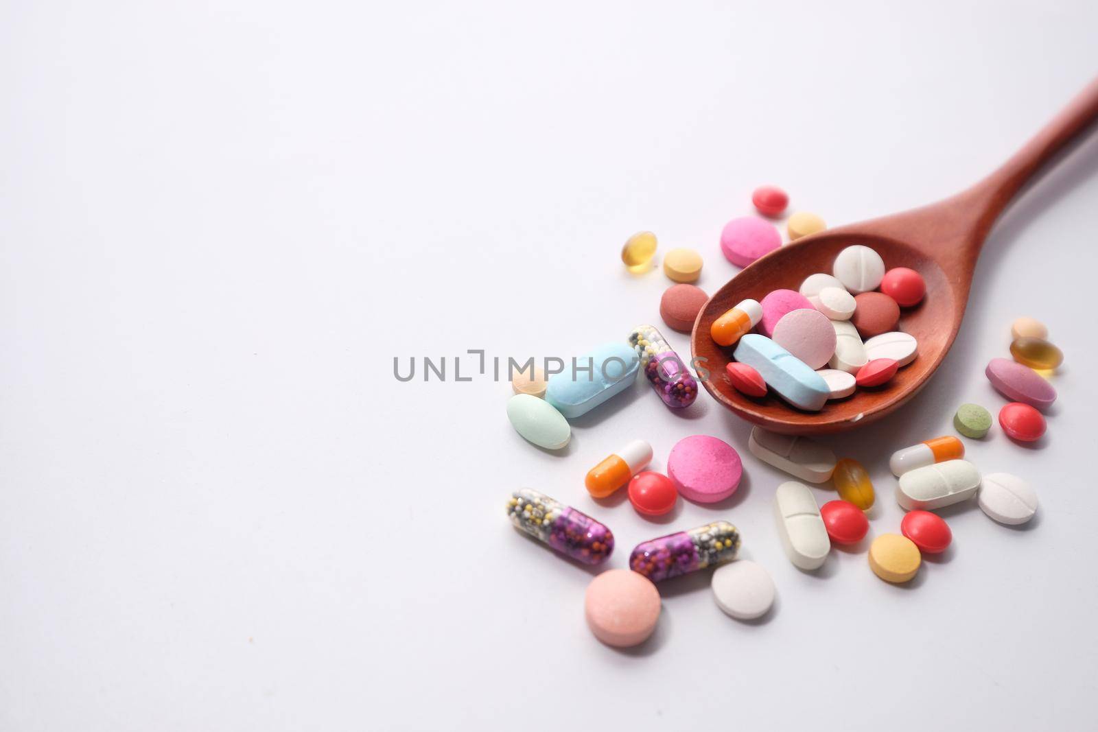 Close up of many colorful pills on spoon on white background .