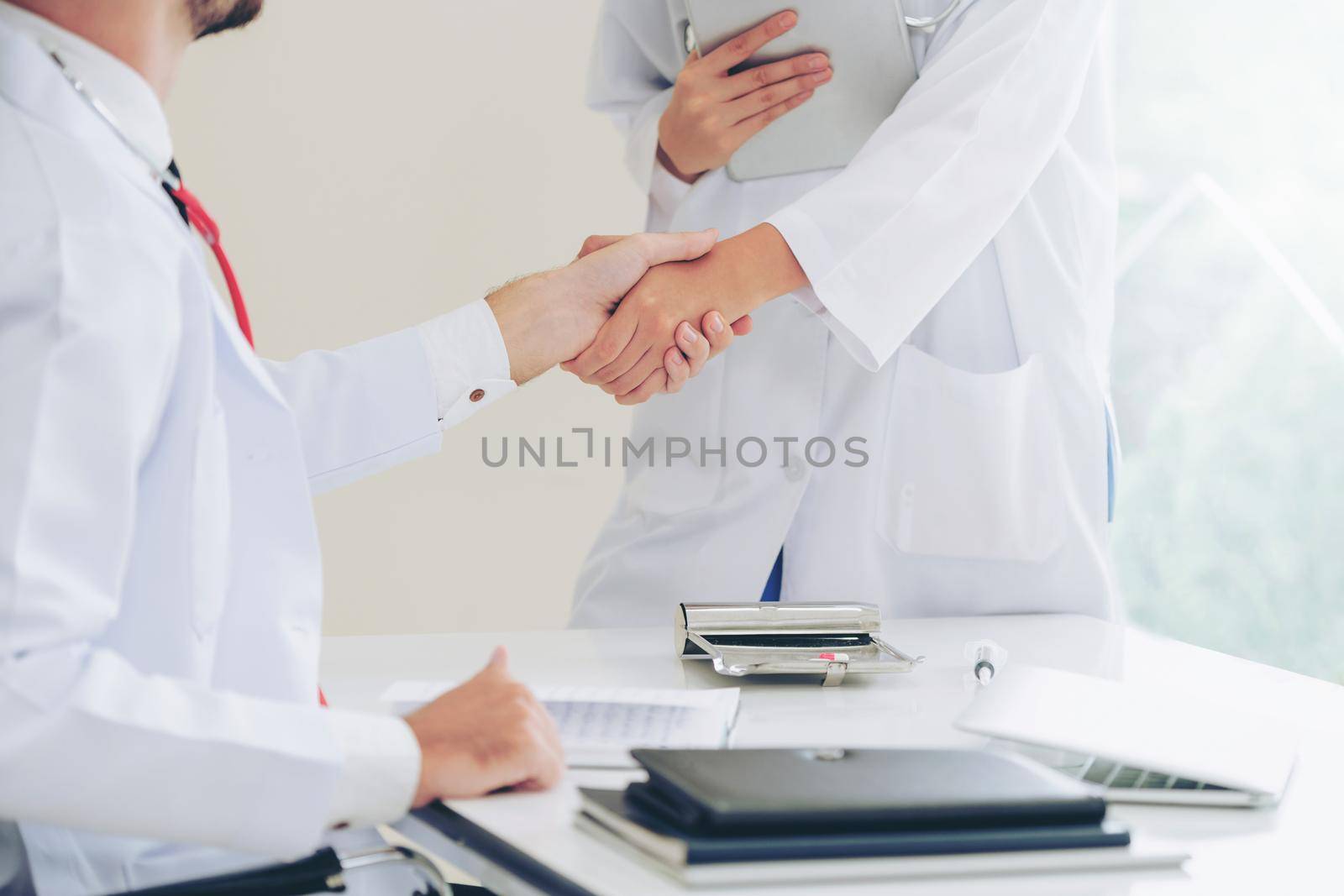 Doctor at the hospital giving handshake to another doctor showing success and teamwork of professional healthcare staff.