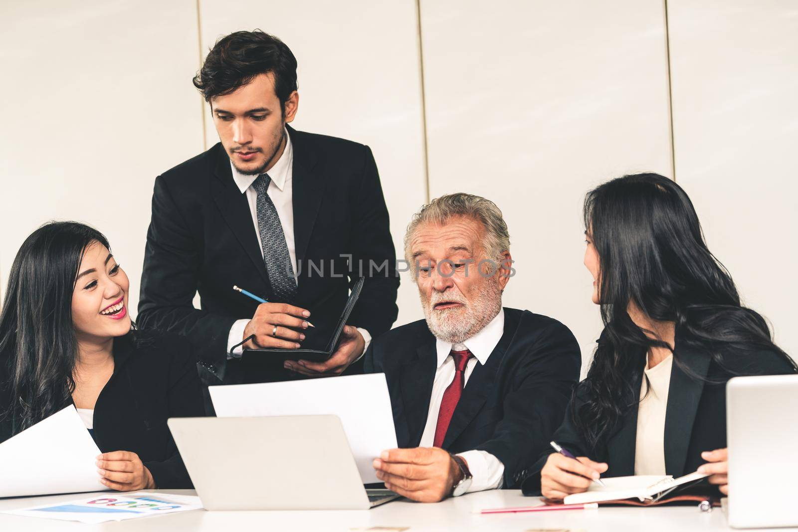 Senior caucasian manager working in office with assistance of young Asian business people and translator in the meeting. Corporate international business and secretary language translation concept.