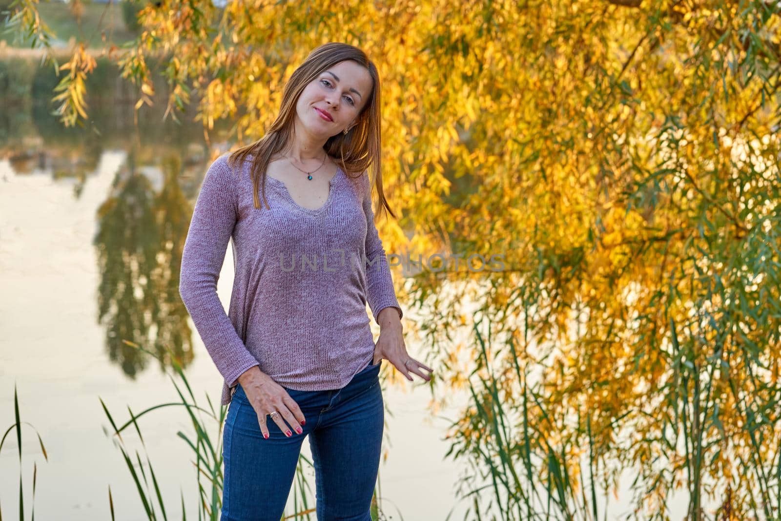 Young cheerful woman in jeans on the shore of the lake with autumnal foliage by jovani68