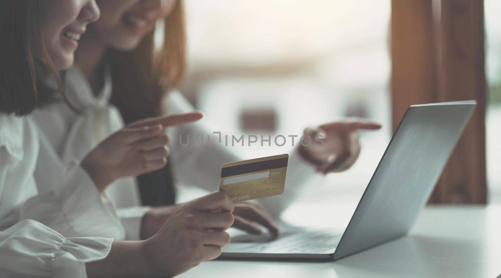 Two young asian women holding credit card and using laptop computer for shopping on line with happiness, business and technology concept, digital marketing, casual lifestyle.