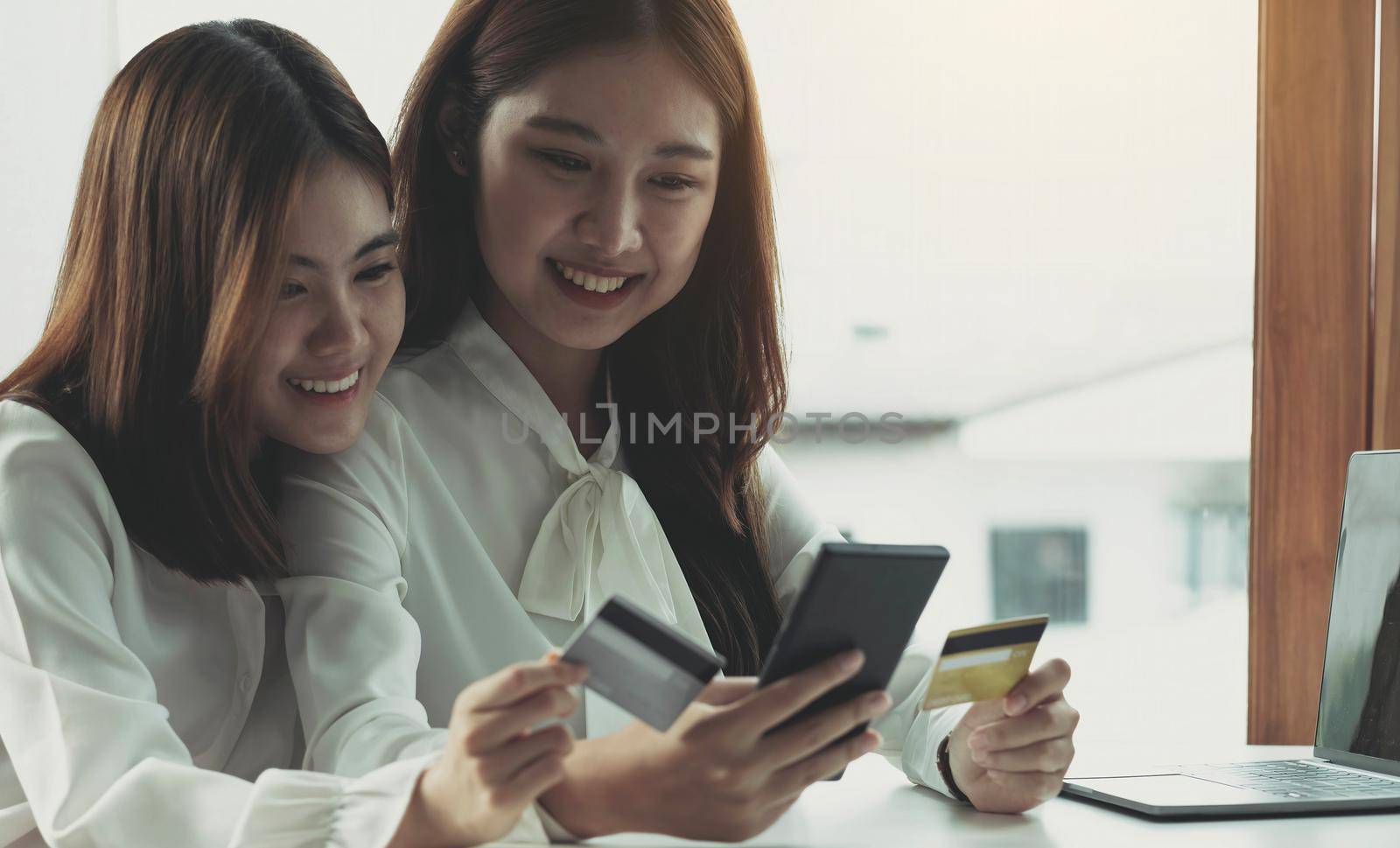 Two young Asian women hold credit cards and happily use their mobile phones for online shopping. business concept and technology digital marketing casual lifestyle