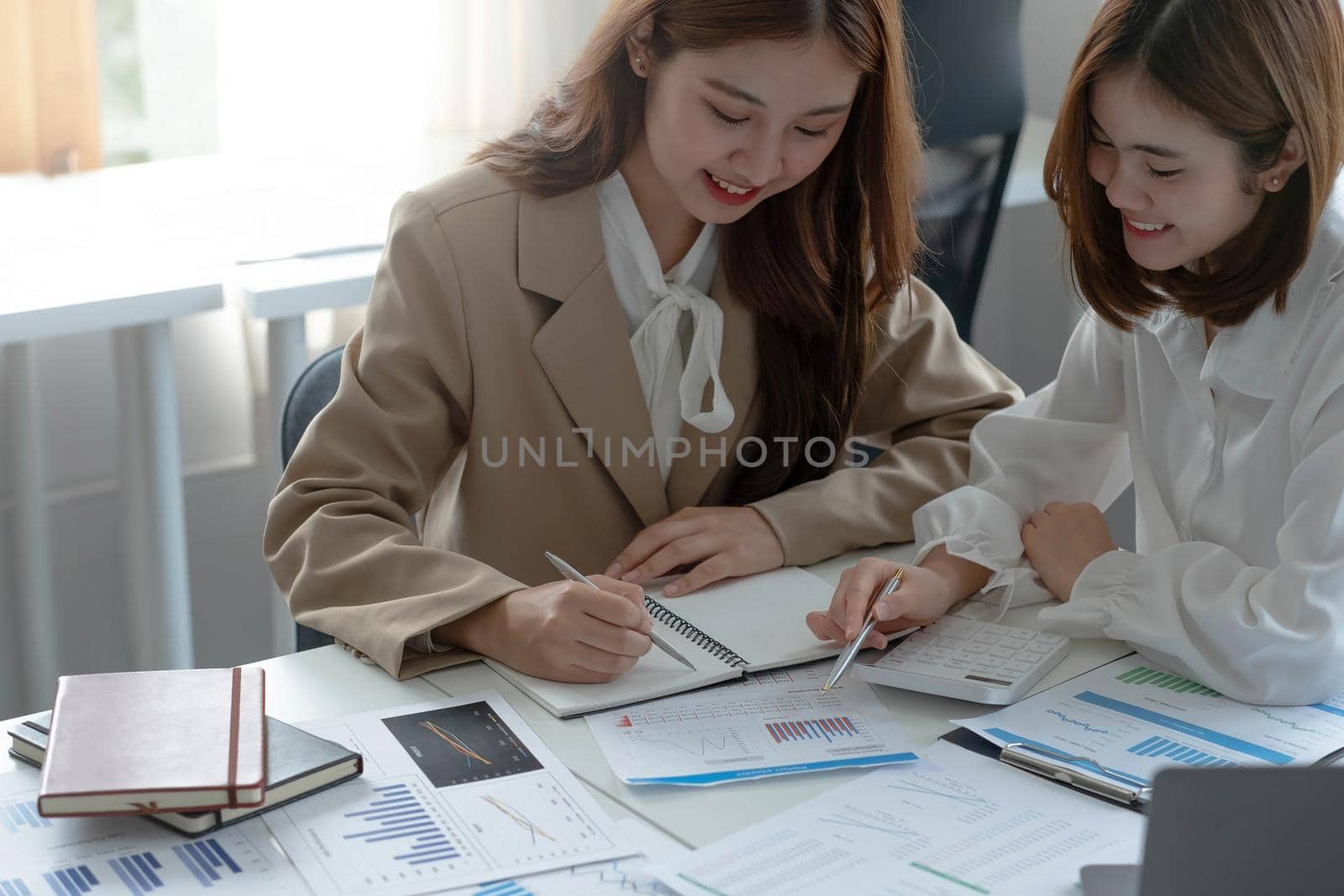 Young Asian businesswoman work together to analysis from work at the office. by wichayada