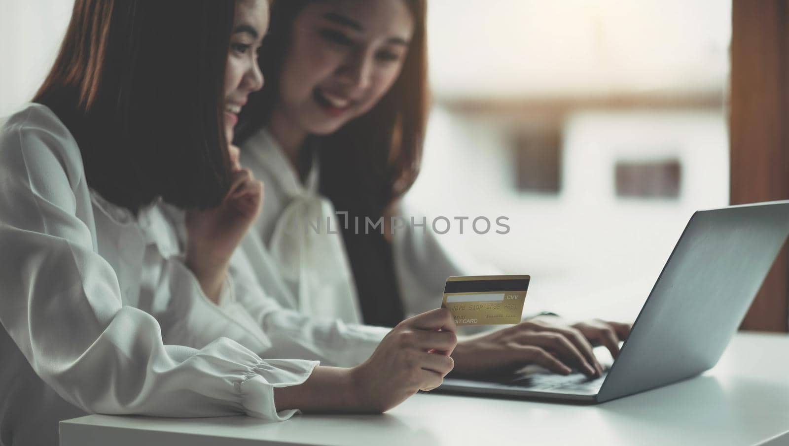 Two young asian women holding credit card and using laptop computer for shopping on line with happiness, business and technology concept, digital marketing, casual lifestyle by wichayada