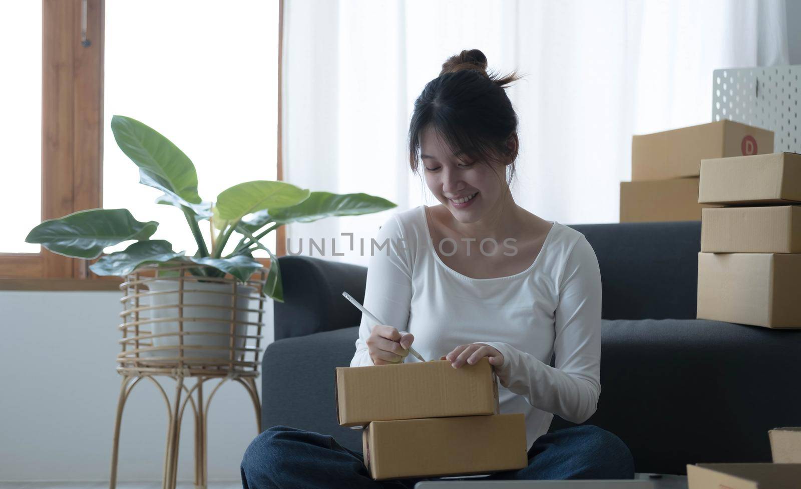 Smiling young Asian business owner woman prepare parcel box and standing check online orders of product for deliver to customer on laptop computer. Shopping Online concept. by wichayada