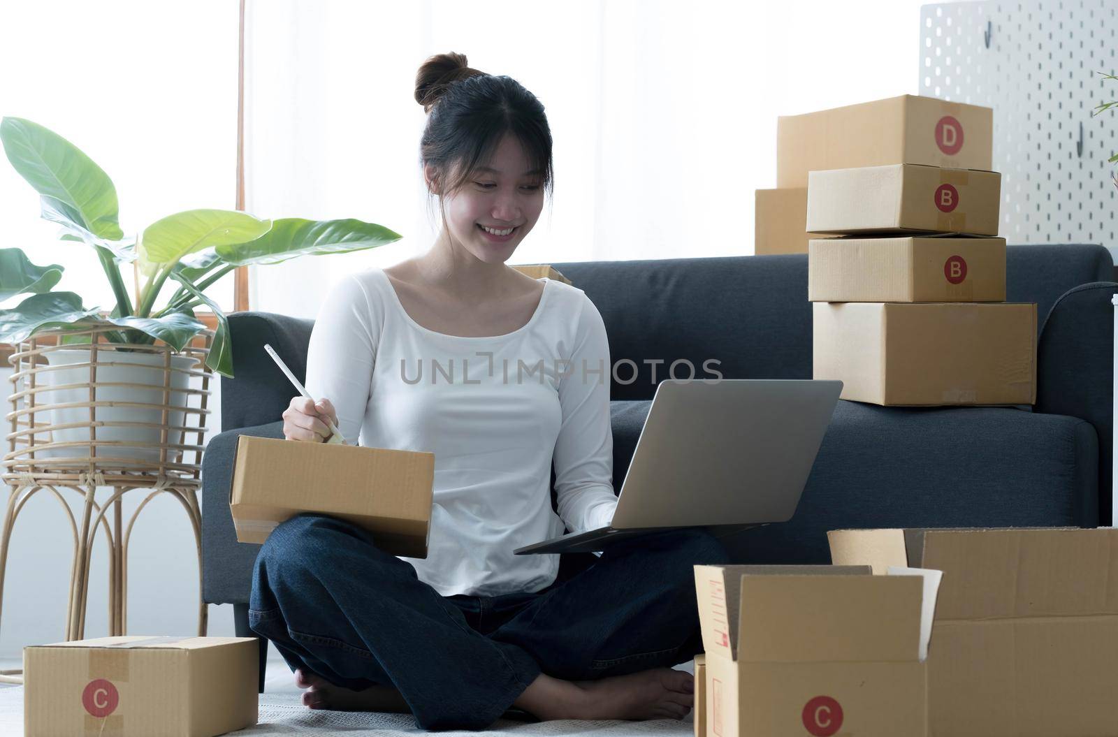 Smiling young Asian business owner woman prepare parcel box and standing check online orders of product for deliver to customer on laptop computer. Shopping Online concept. by wichayada