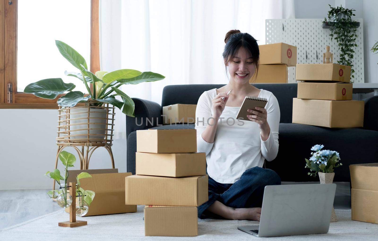 Smiling young Asian business owner woman prepare parcel box and standing check online orders of product for deliver to customer on laptop computer. Shopping Online concept. by wichayada