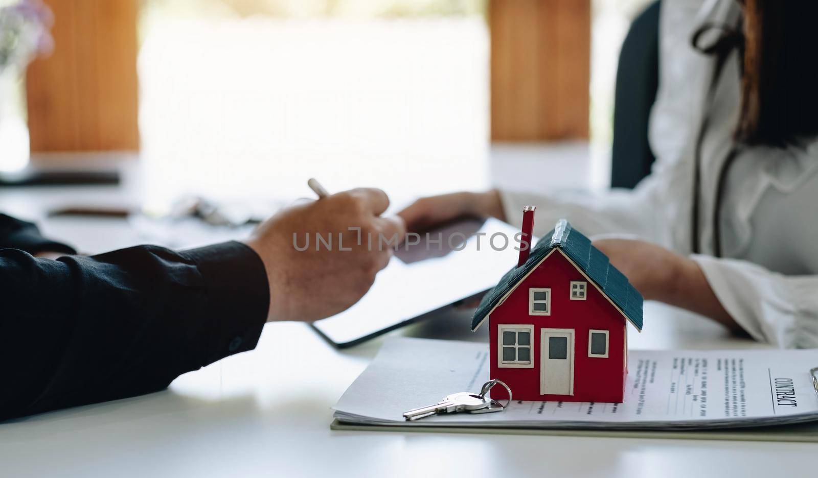 Real estate agent with house model hand putting signing contract,have a contract in place to protect it,signing of modest agreements form in office.Concept real estate,moving home or renting property by wichayada