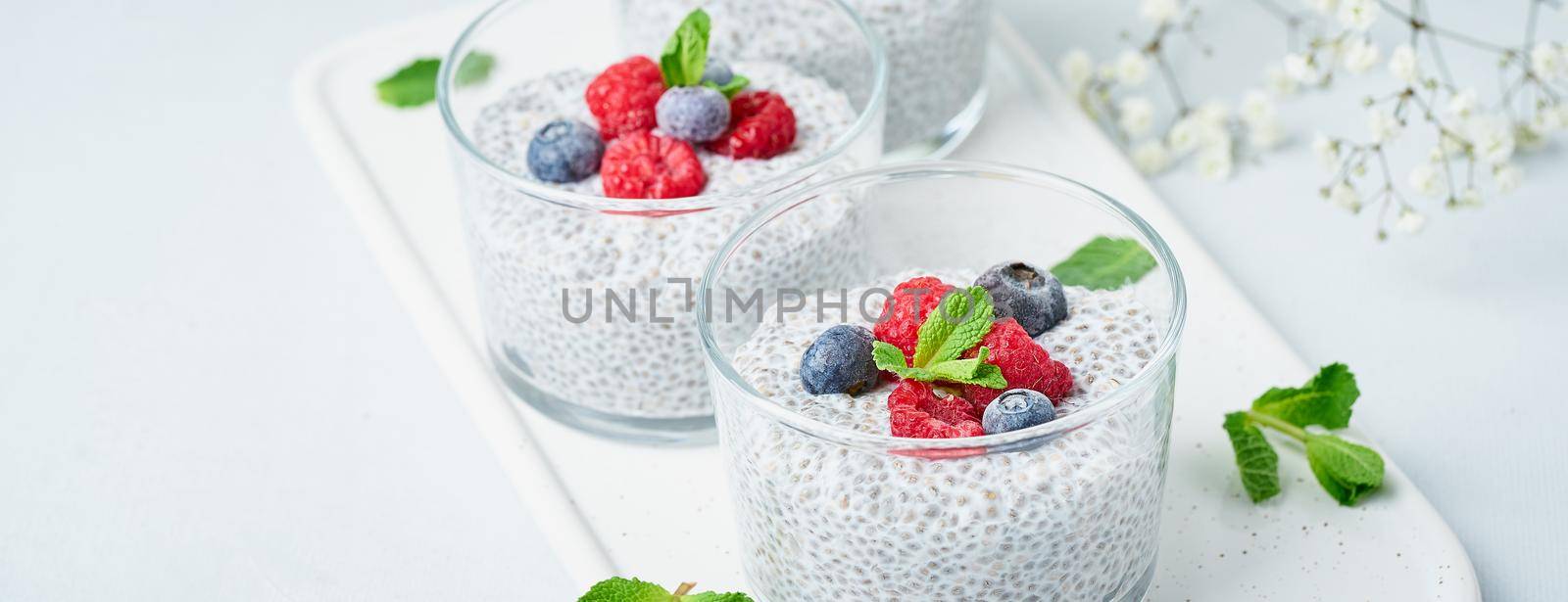 Banner with chia pudding with fresh berries raspberries, blueberries. Three glass, light background, side view, flowers