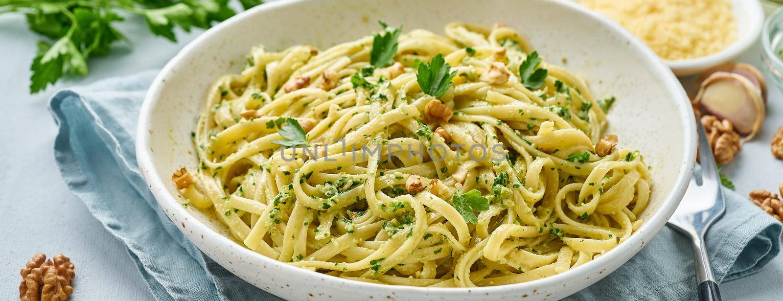 Banner with pesto pasta, bavette with walnuts, parsley, garlic, nuts, olive oil. Side view, long side, blue background