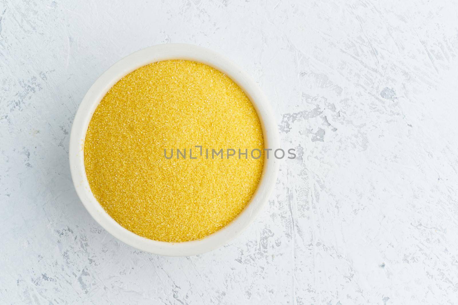 Corn, polenta in a white bowl on white background. Dried cereals in cup, vegan food, fodmap diet. Top view, close up.