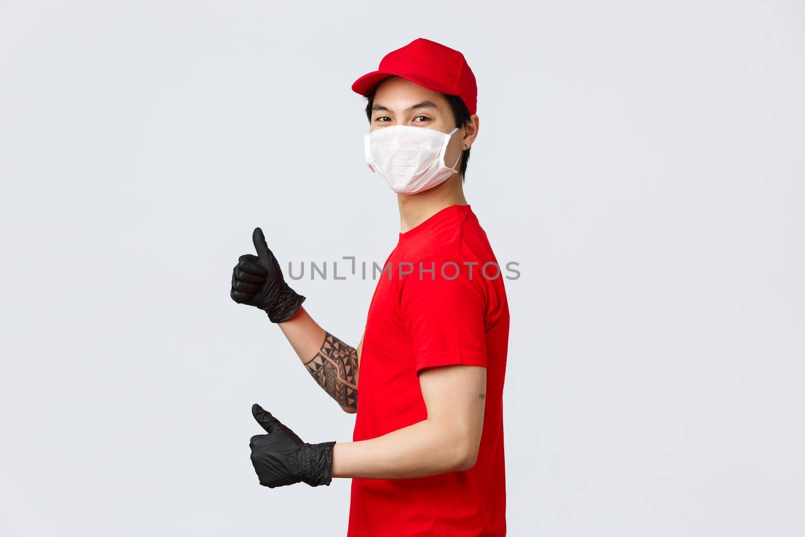 Best delivery service. Delivery guy in red cap and t-shirt, logistic company employee show thumbs-up, standing profile and turn camera with protective medical mask, gloves, recommend courier service.
