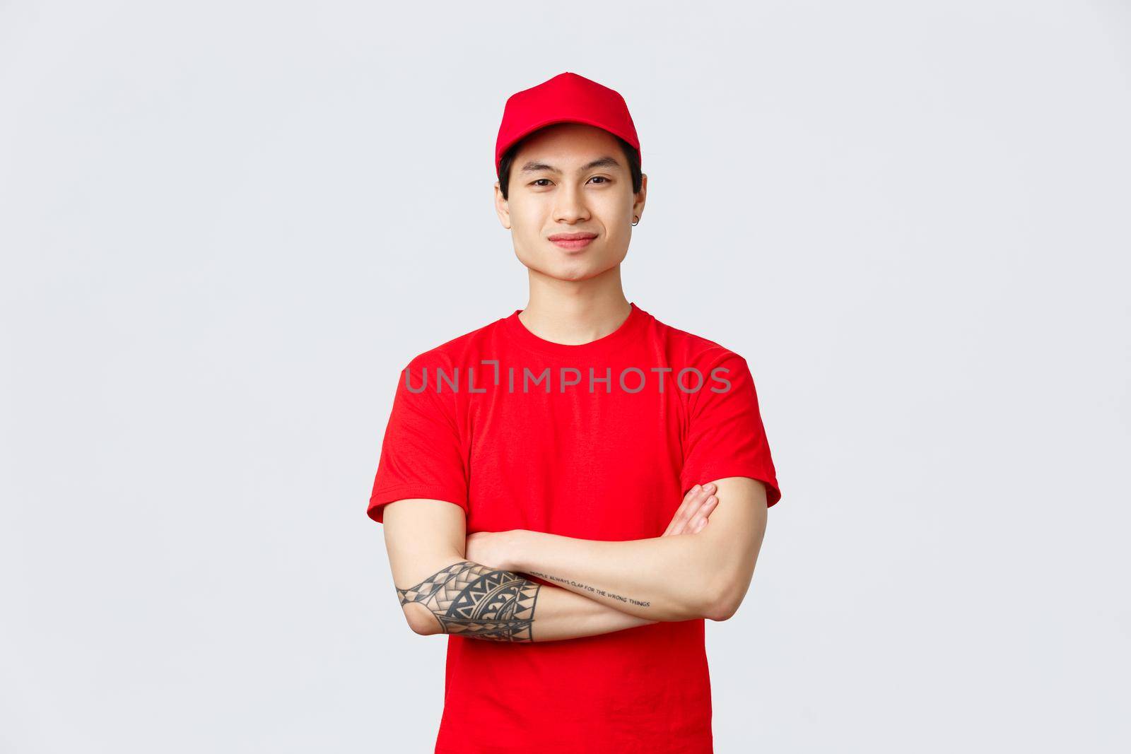 Express delivery, shipping and logistics concept. Confident asian man working in deliver company, wearing red uniform with cap and t-shirt, cross arms chest and smiling.