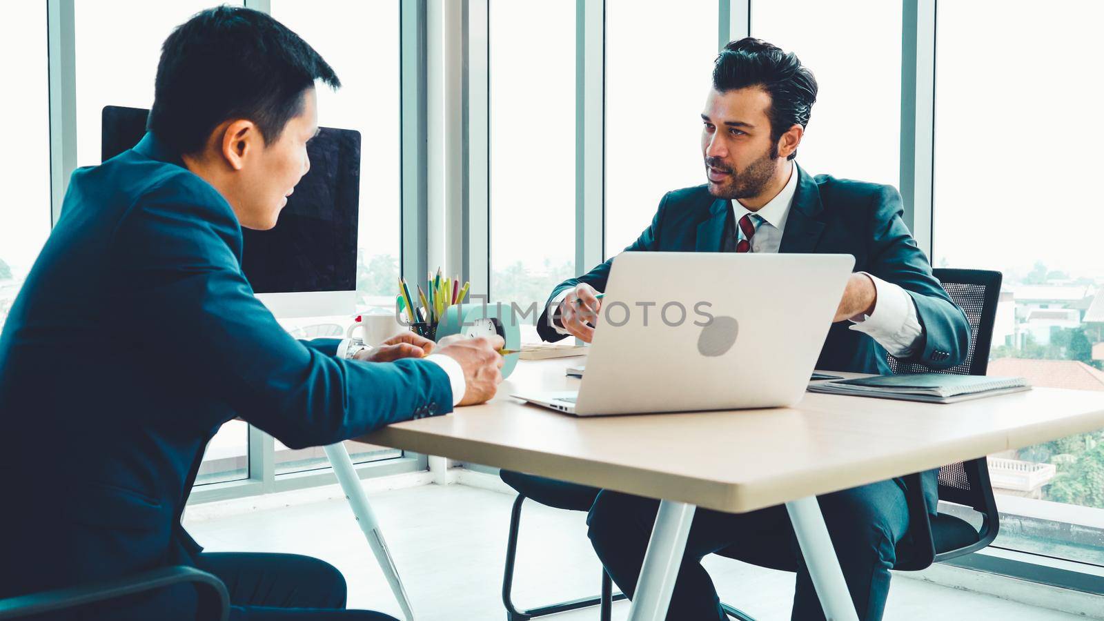 Two business people talk project strategy at office meeting room. Businessman discuss project planning with colleague at modern workplace while having conversation and advice on financial data report.