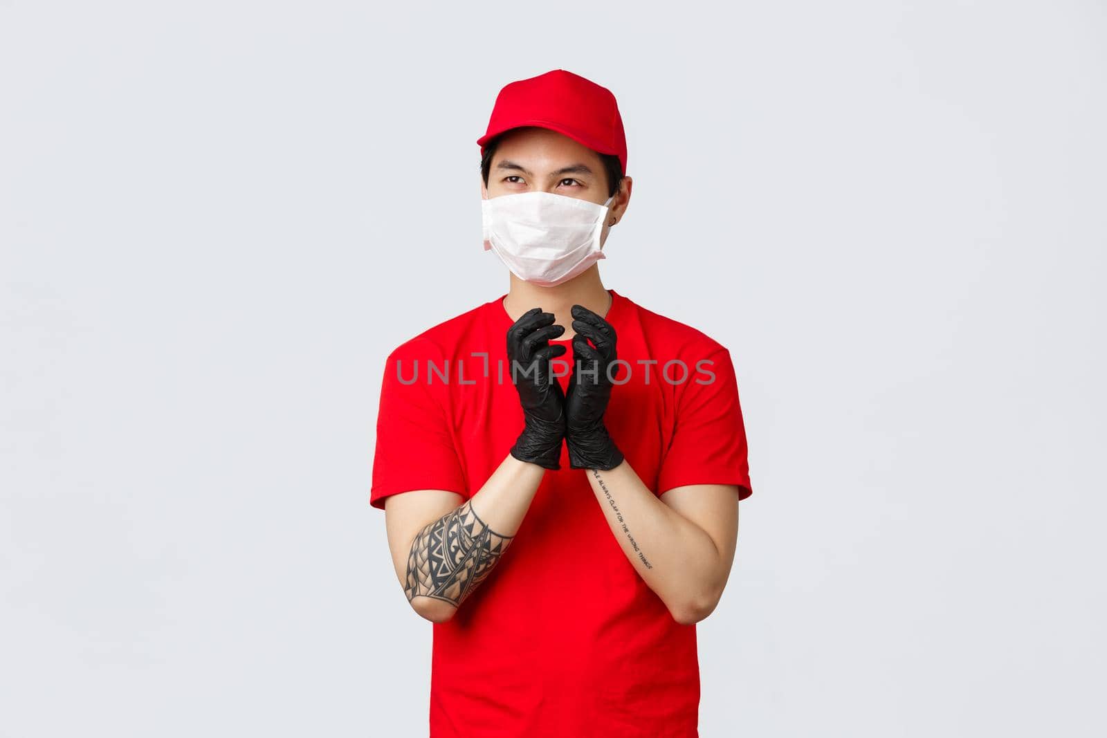 Creative asian delivery guy making plan, sheming something, have interesting thought in mind, steeple fingers in protective gloves, look away pondering idea, protect health with medical mask.
