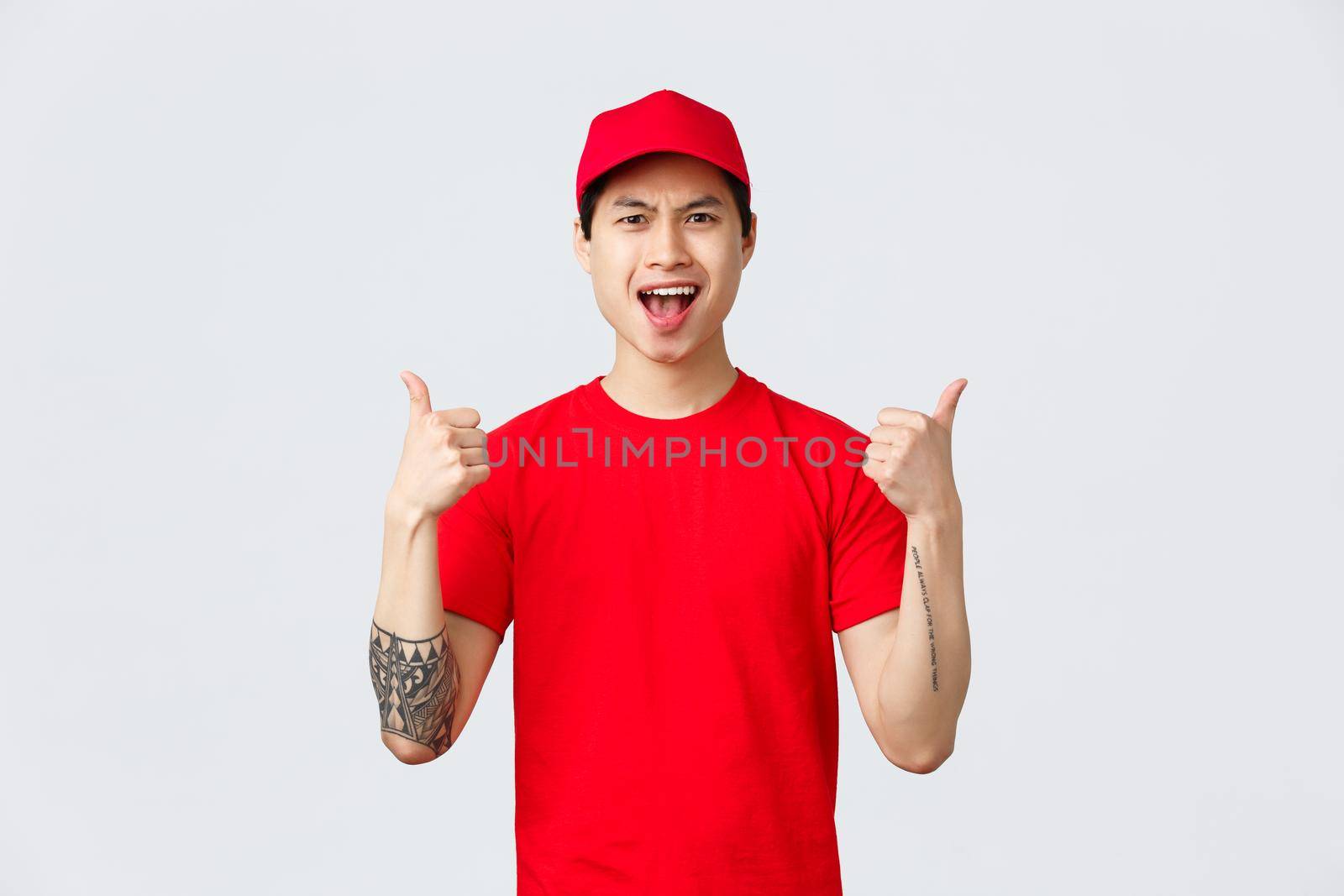 Express delivery, shipping and logistics concept. Upbeat handsome asian courier in red t-shirt and cap, show thumbs-up, encourage keep up good work, being the best, chanting in celebration.