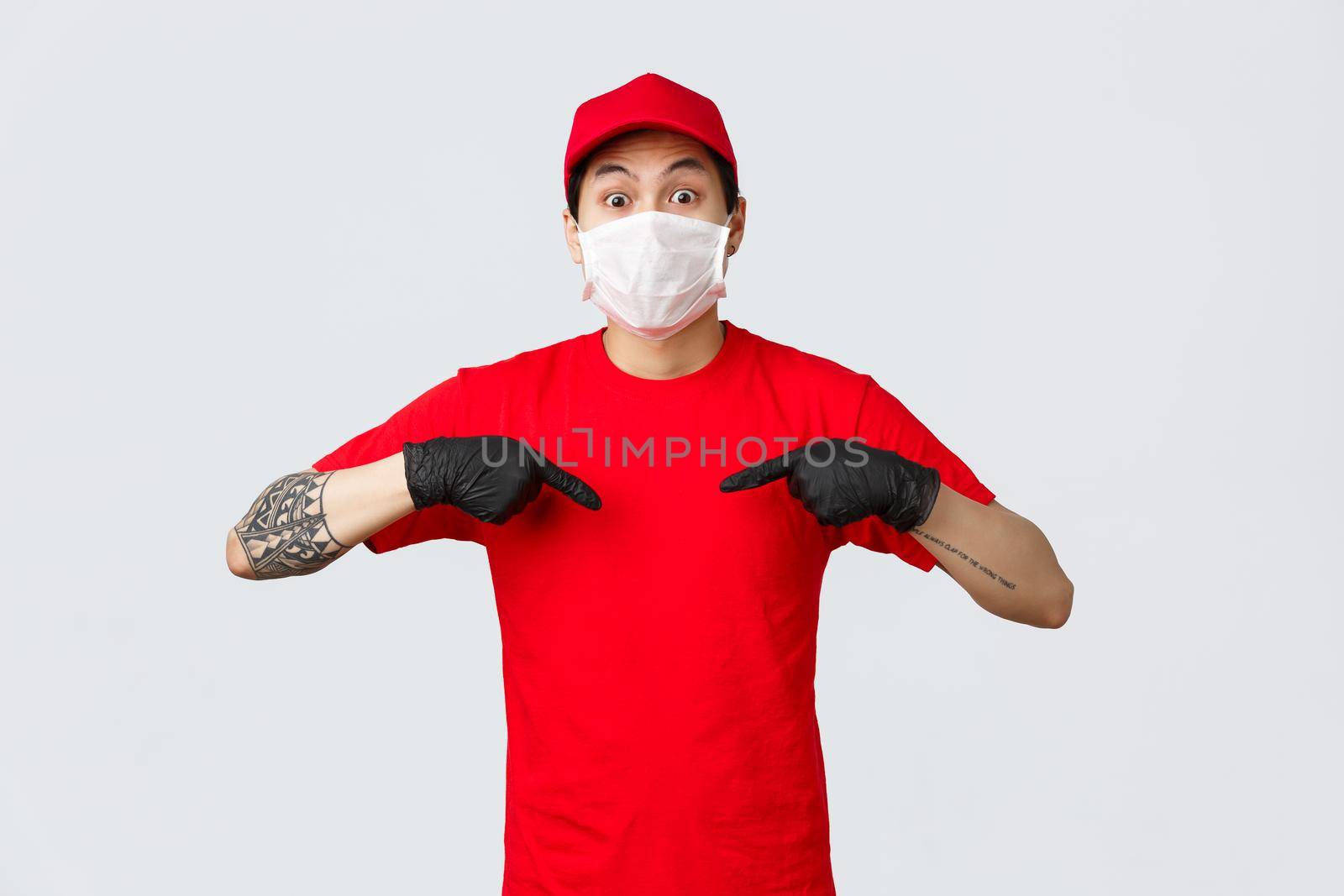 Surprised gasping asian delivery man in red cap and t-shirt, wearing protective mask and medical gloves to prevent virus spread, care for customers safety during self-qurantine online orders delivery.