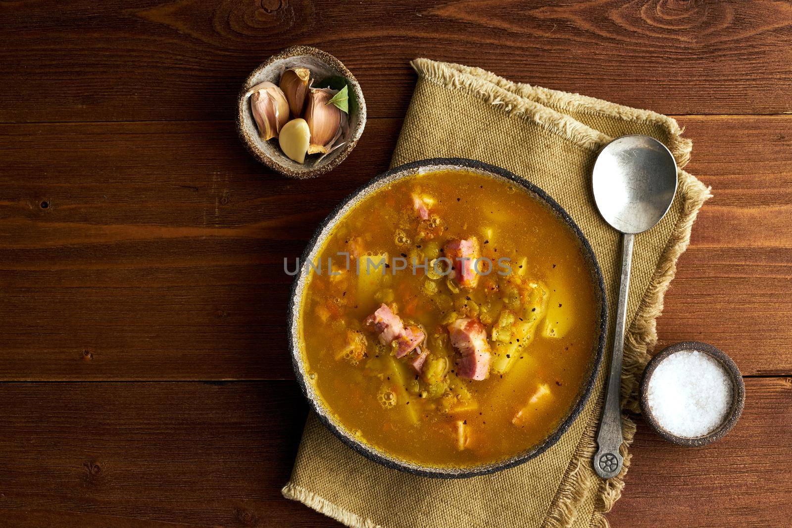 Winter hot soup with chopped green peas, pork, bacon, smoked on a dark brown wooden table. Delicious appetizing fat rich soup, copy space
