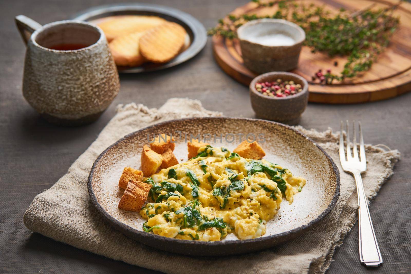 Scrambled eggs with spinach, cup of tea on dark brown background. Breakfast with Pan-fried omelette, side view, close up